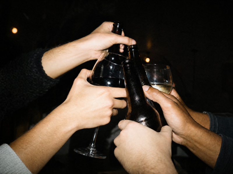 Hands clinking bottles and glasses in a toast