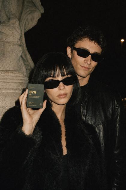 A couple out on the street at night, holding a box of SYN